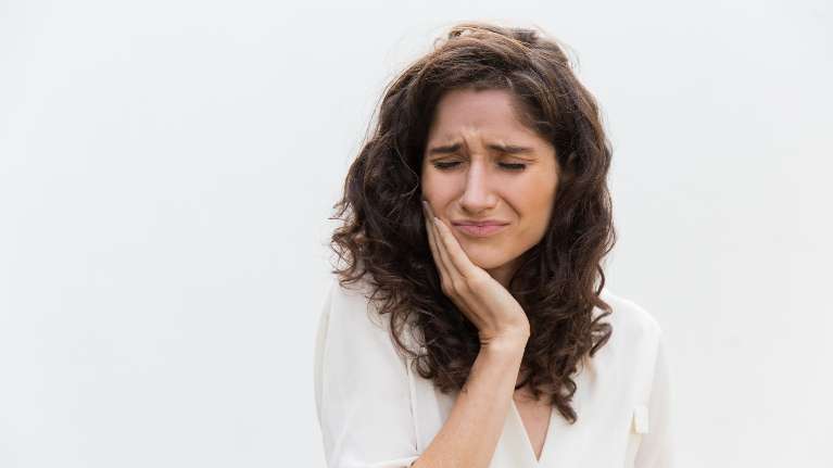 A concerned woman covers her mouth, indicating worry about her dental health and the need for care.