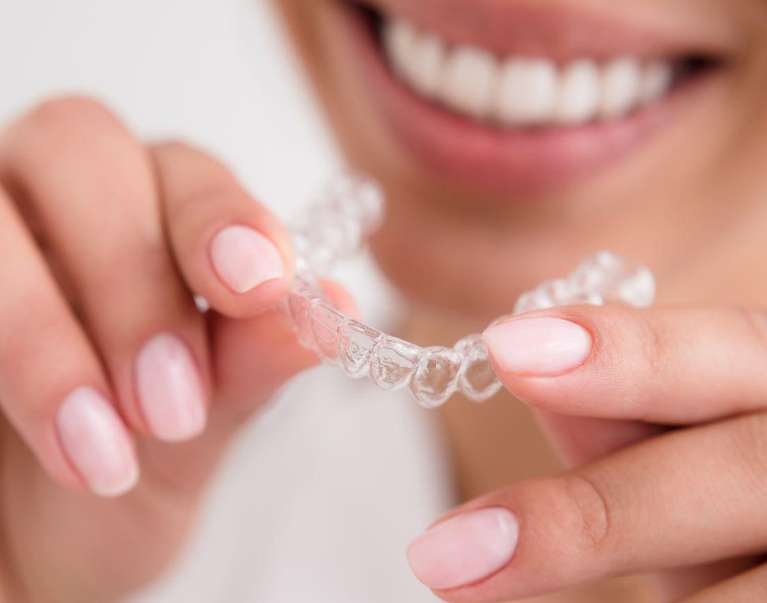A woman holds a clear aligner, showcasing Invisalign®'s transformative power for her smile.
