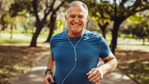 Smiling older man jogging in a park, looking healthy and active after dental bone grafting recovery